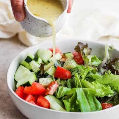 Homemade salad dressing getting poured over large bowl of salad