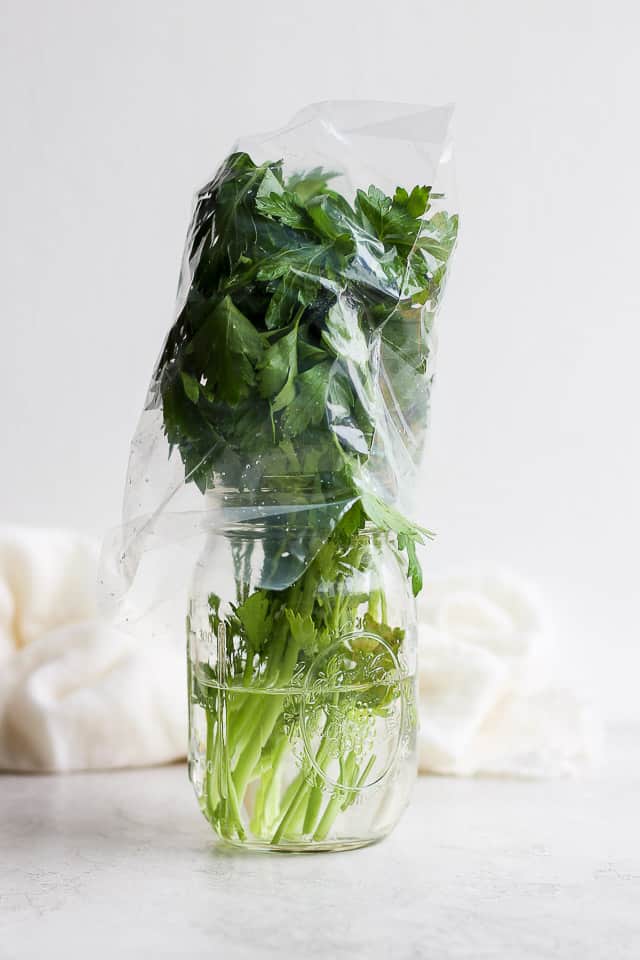 Bunch of parsley in a clear mason jar covered with plastic wrap