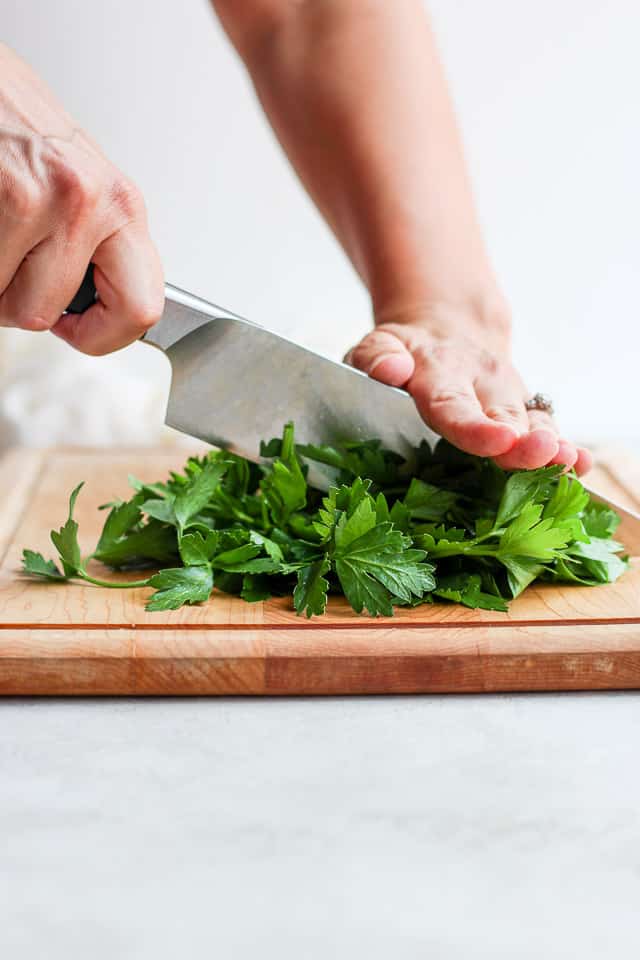 Hand chopping parsley on wooden cutting board
