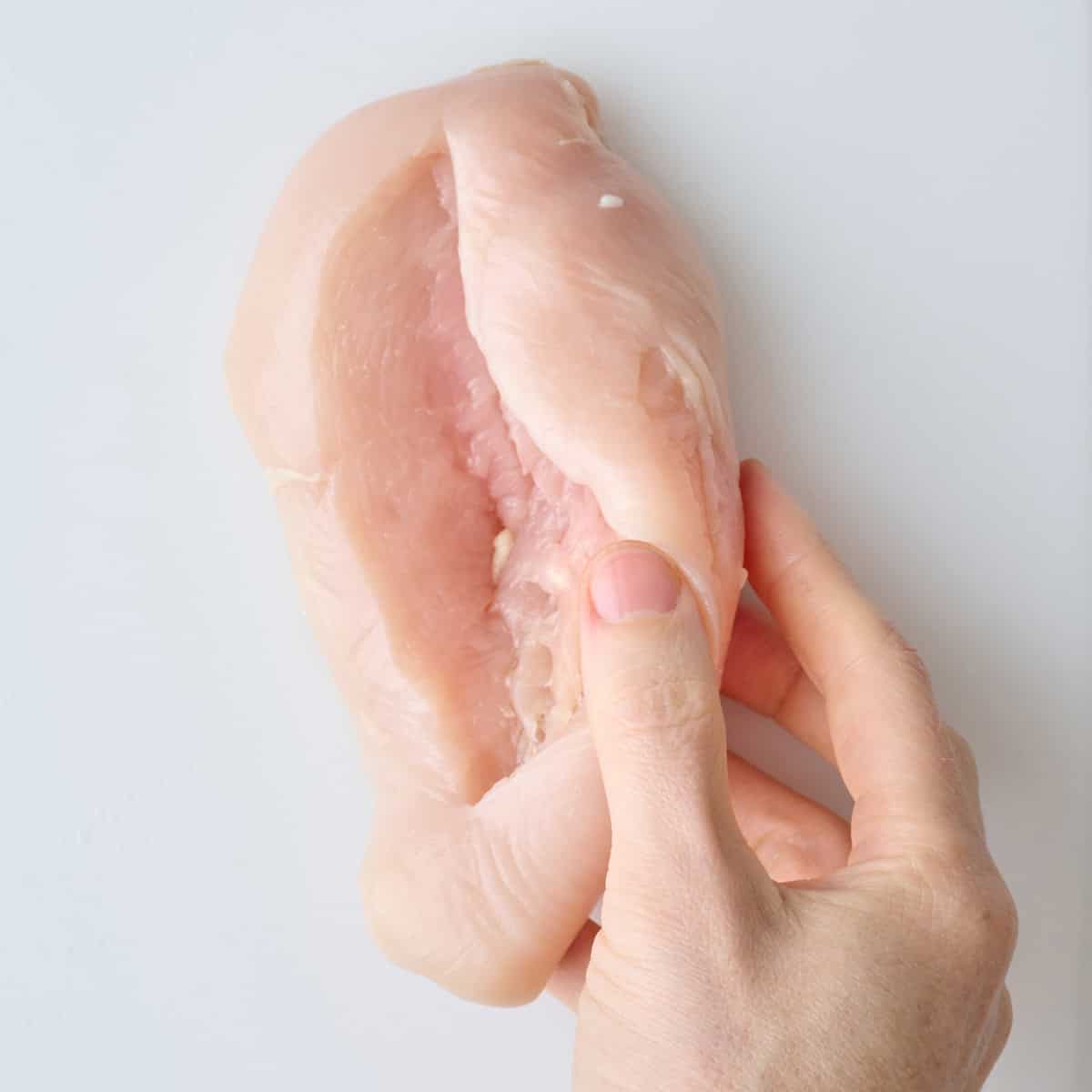 A hand holding a chicken breast after slicing a horizontal cut through the thickest part to create a pocket.