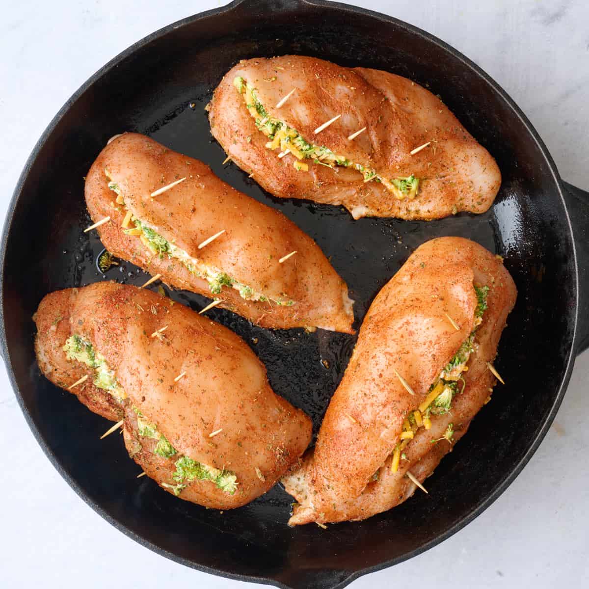 Stuffed chicken breasts in a skillet closed with toothpicks before cooking.