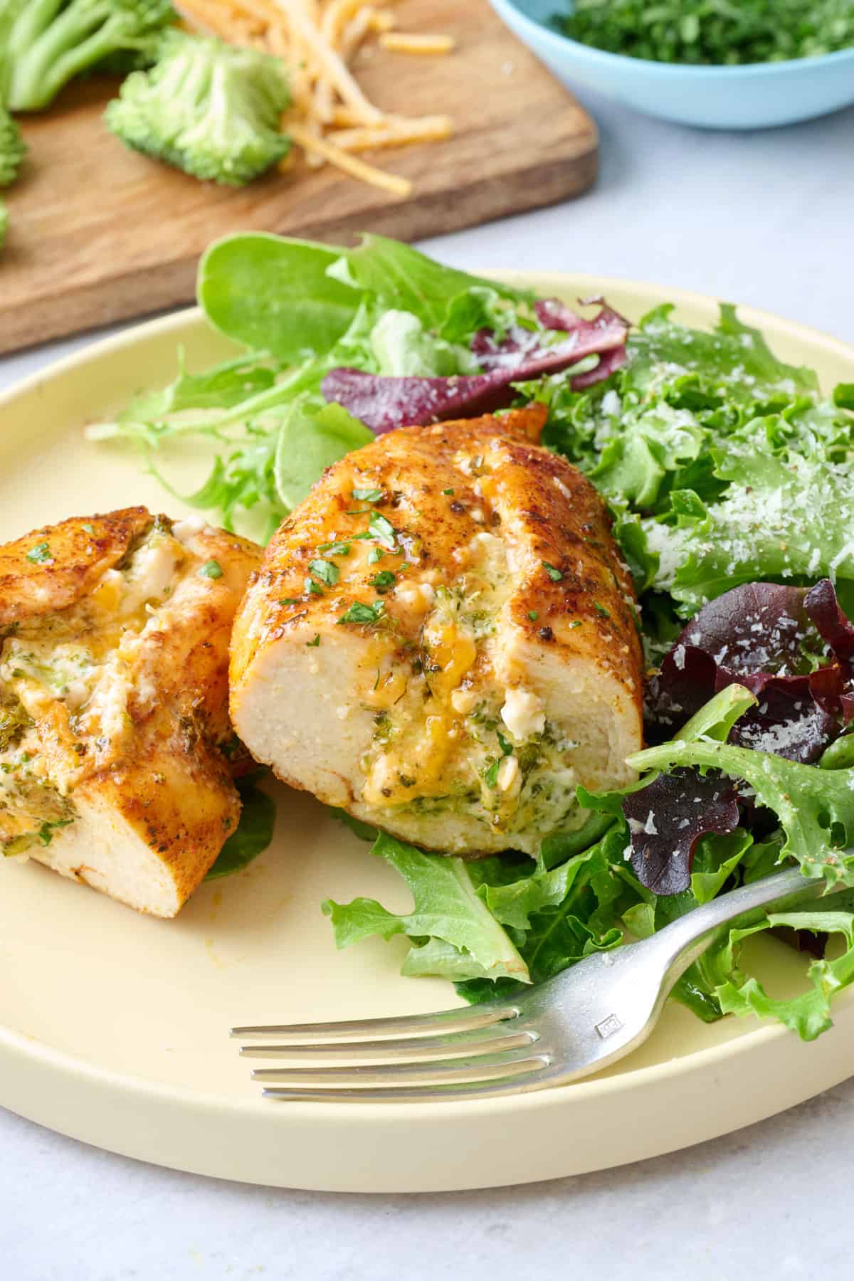 One chicken breast on a plate served with a light spring mix salad, cut in half.