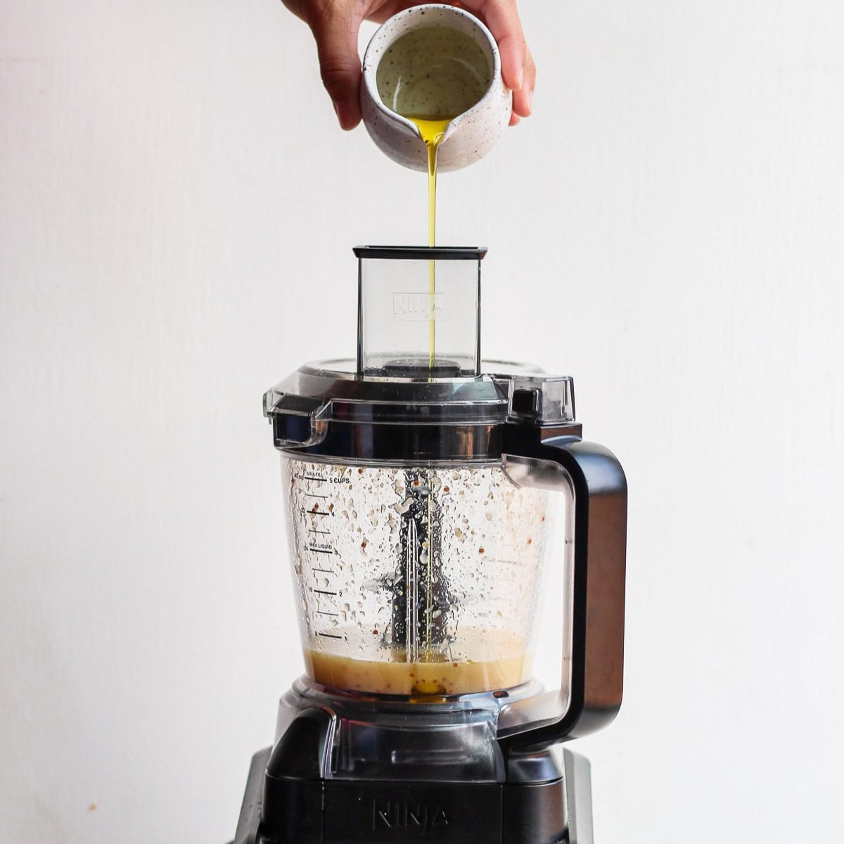 Pouring olive oil into the processor.