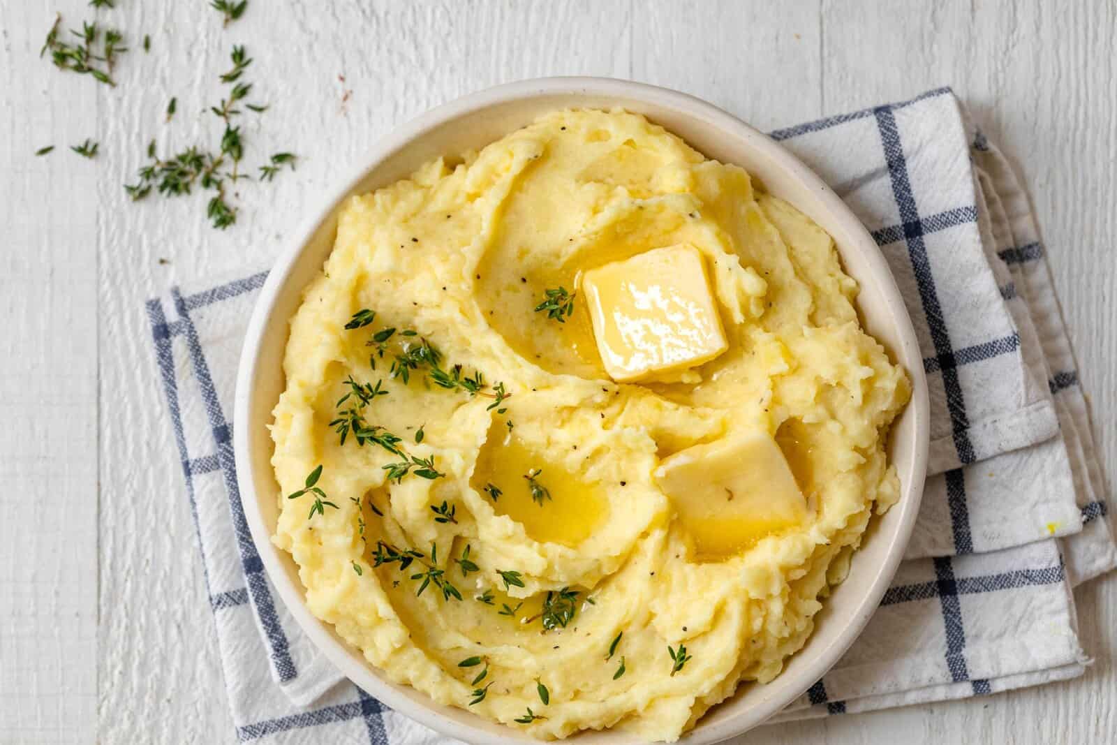 A bowl of instant pot mashed potatoes with garnish and butter.