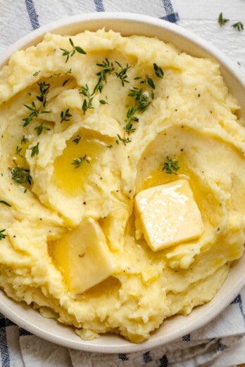 A bowl of instant pot mashed potatoes with garnish and butter.