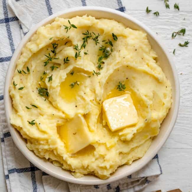 A bowl of instant pot mashed potatoes with garnish and butter.