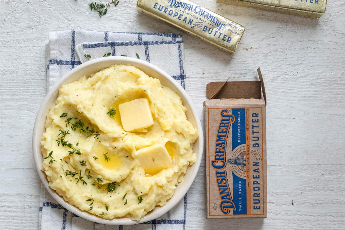 Mashed potatoes made in instant pot served in while bowl shown with Danish Creamery butter package next to it