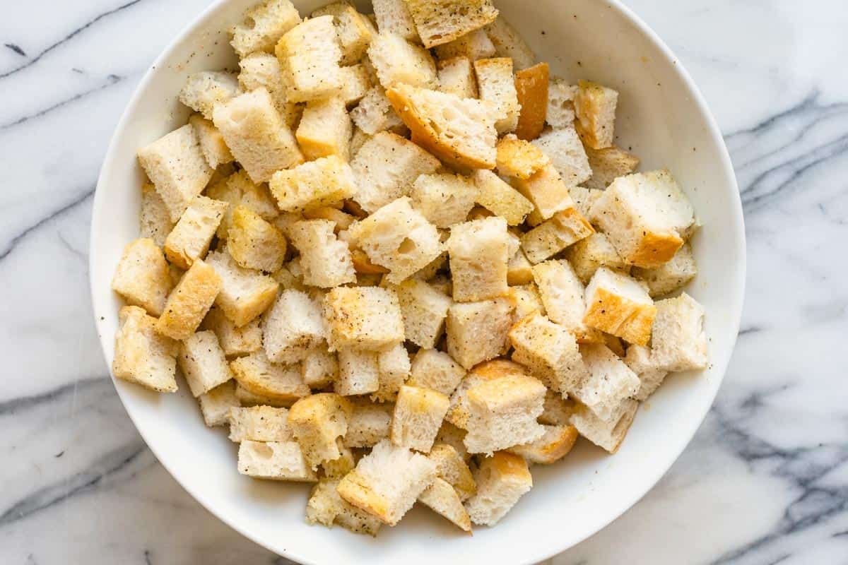 Sourdough bread cut into cubes in large bowl coated with oil and seasoning