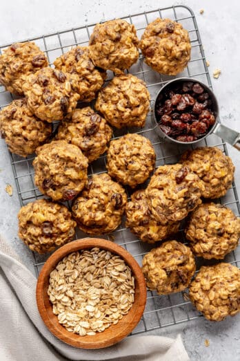 Oatmeal breakfast cookies on a wire rack with a small bowl of oats and dried cranberries.