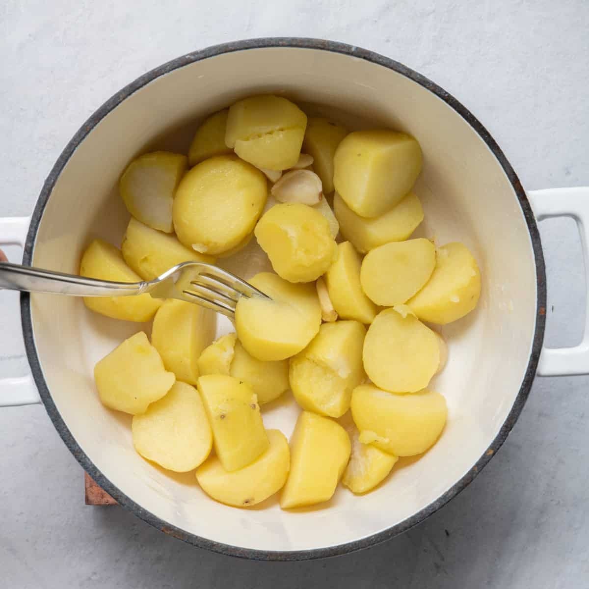 Drained potatoes and garlic back in pot with fork piercing to show tender.