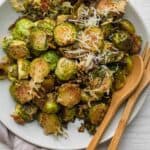 Parmesan brussel sprouts roasted in a large white bowl with a wooden spoon and wooden fork in bowl