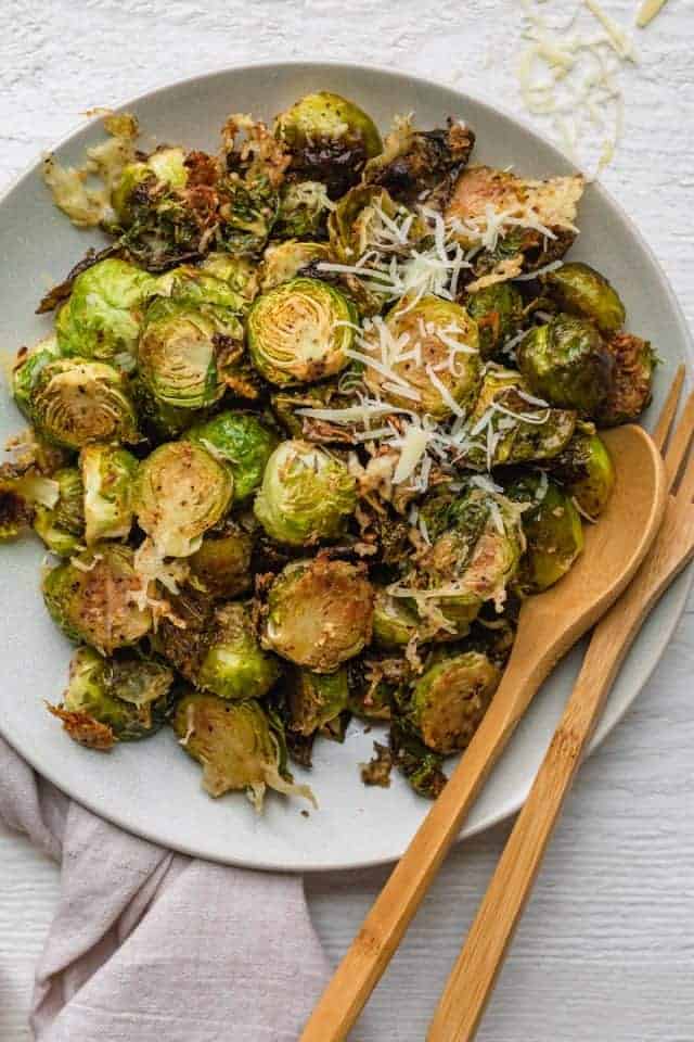 Parmesan brussel sprouts roasted in a large white bowl with a wooden spoon and wooden fork in bowl