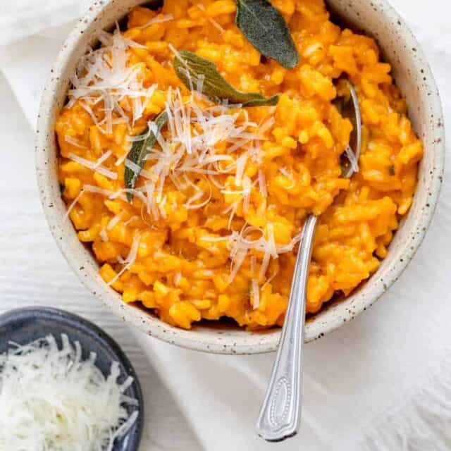 Pumpkin risotto in a small bowl with parmesan cheese on the side