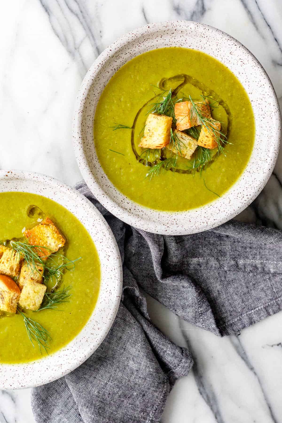 Two bowls of vegan broccoli soup topped with croutons