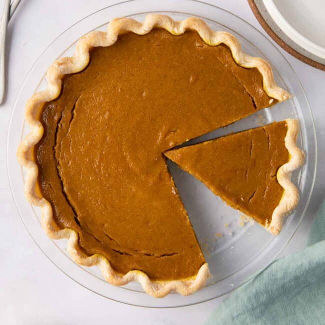 Pumpkin pie with slices cut out in a round glass baking dish.