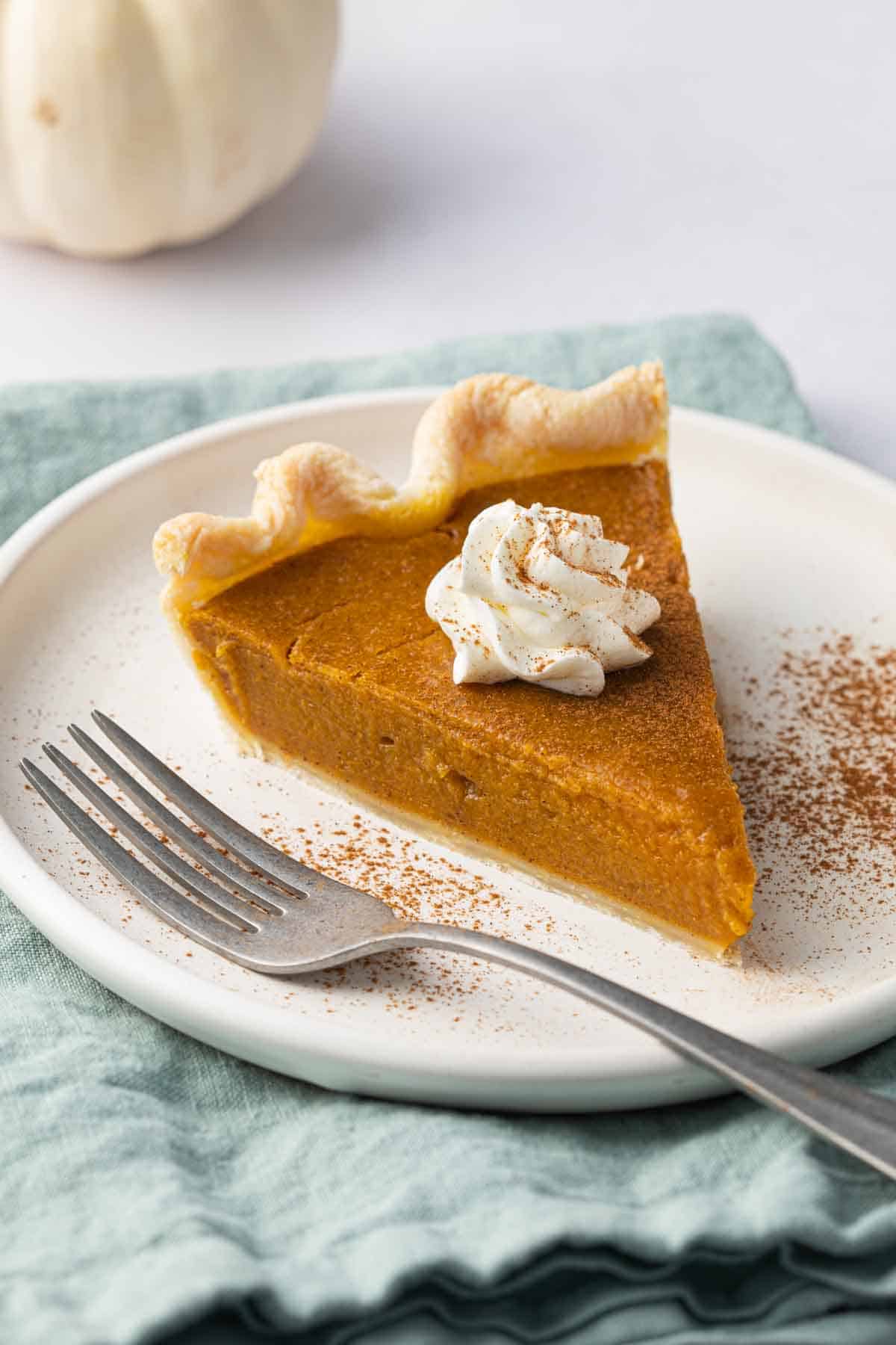 Slice of pumpkin pie on a small plate with whipped cream on top