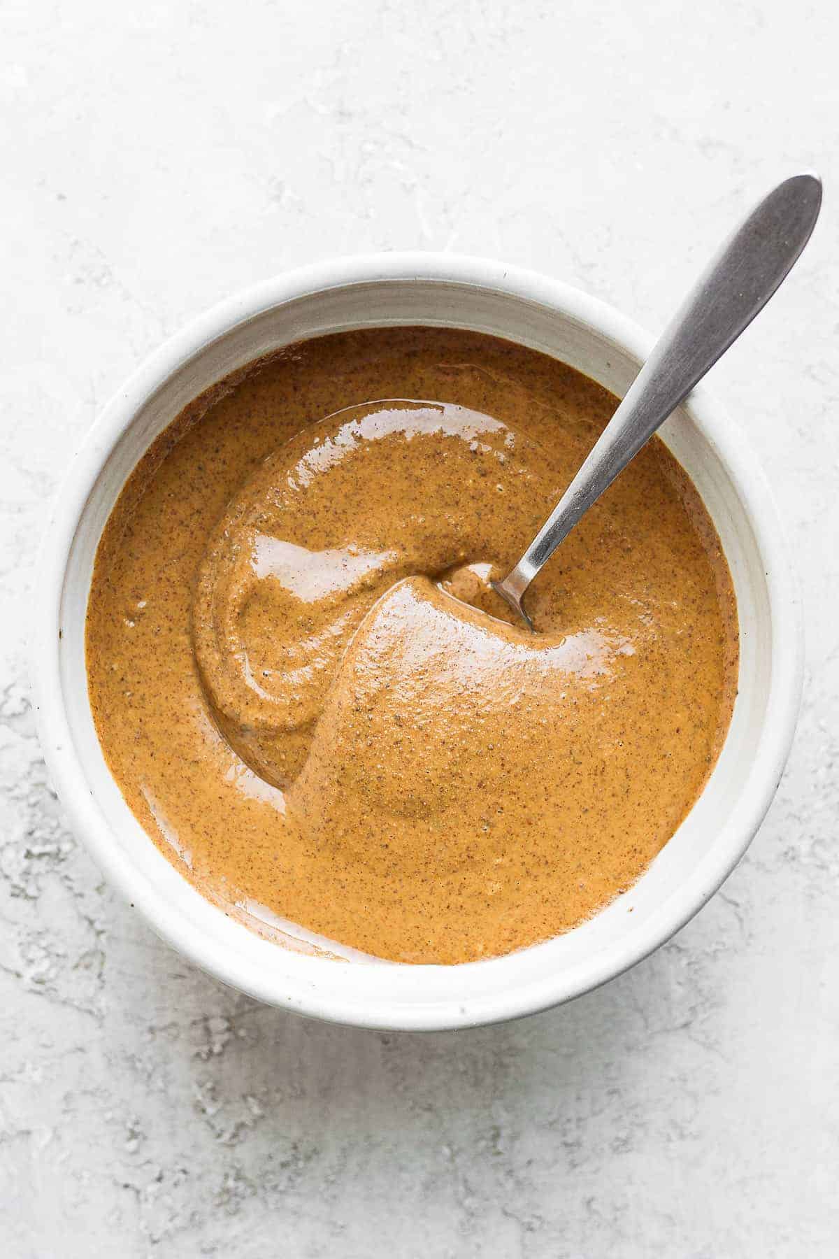 Homemade almond butter in a white bowl with spoon inside