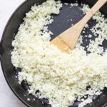 Cooking cauliflower rice in skillet with wooden spatula