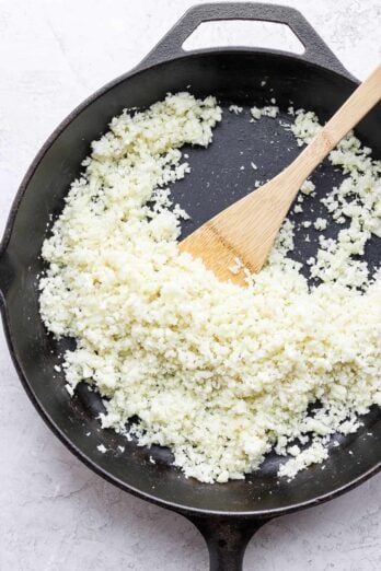 Cooking cauliflower rice in skillet with wooden spatula