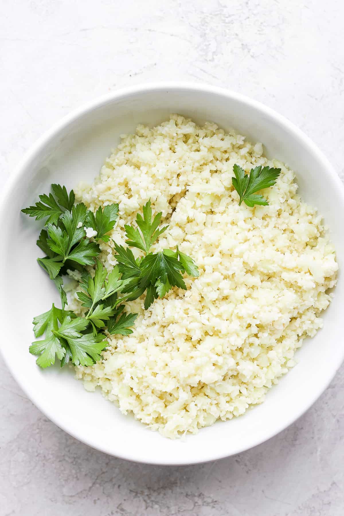 Cooked cauliflower rice in a large bowl with parsley on top