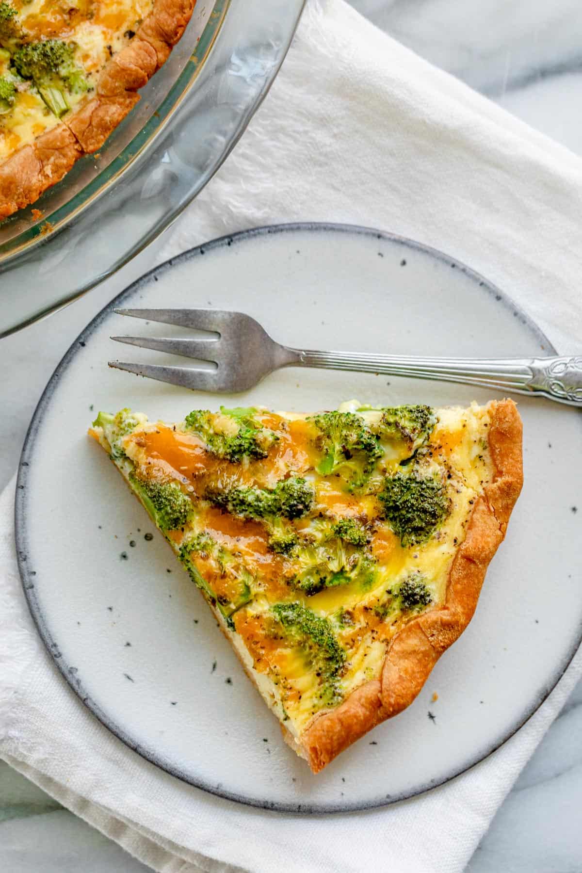 One slice of broccoli and cheese quiche on small plate with fork on the side