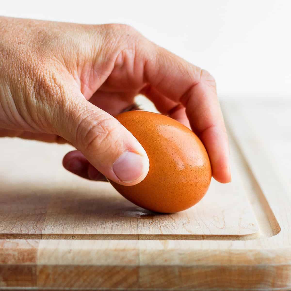 Hand tapping egg on cutting board.
