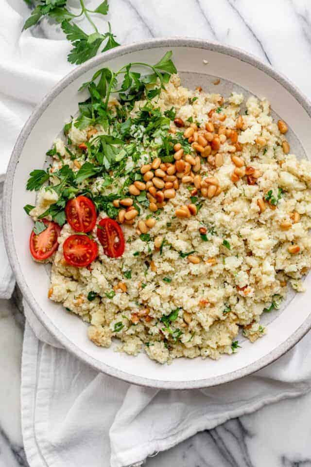 Mediterranean cauliflower rice in a large bowl with parsley and pinenuts