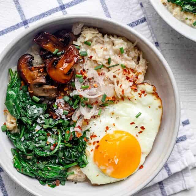 Bowl of savory oatmeal topped with spinach, mushrooms, shallows, and a fried egg