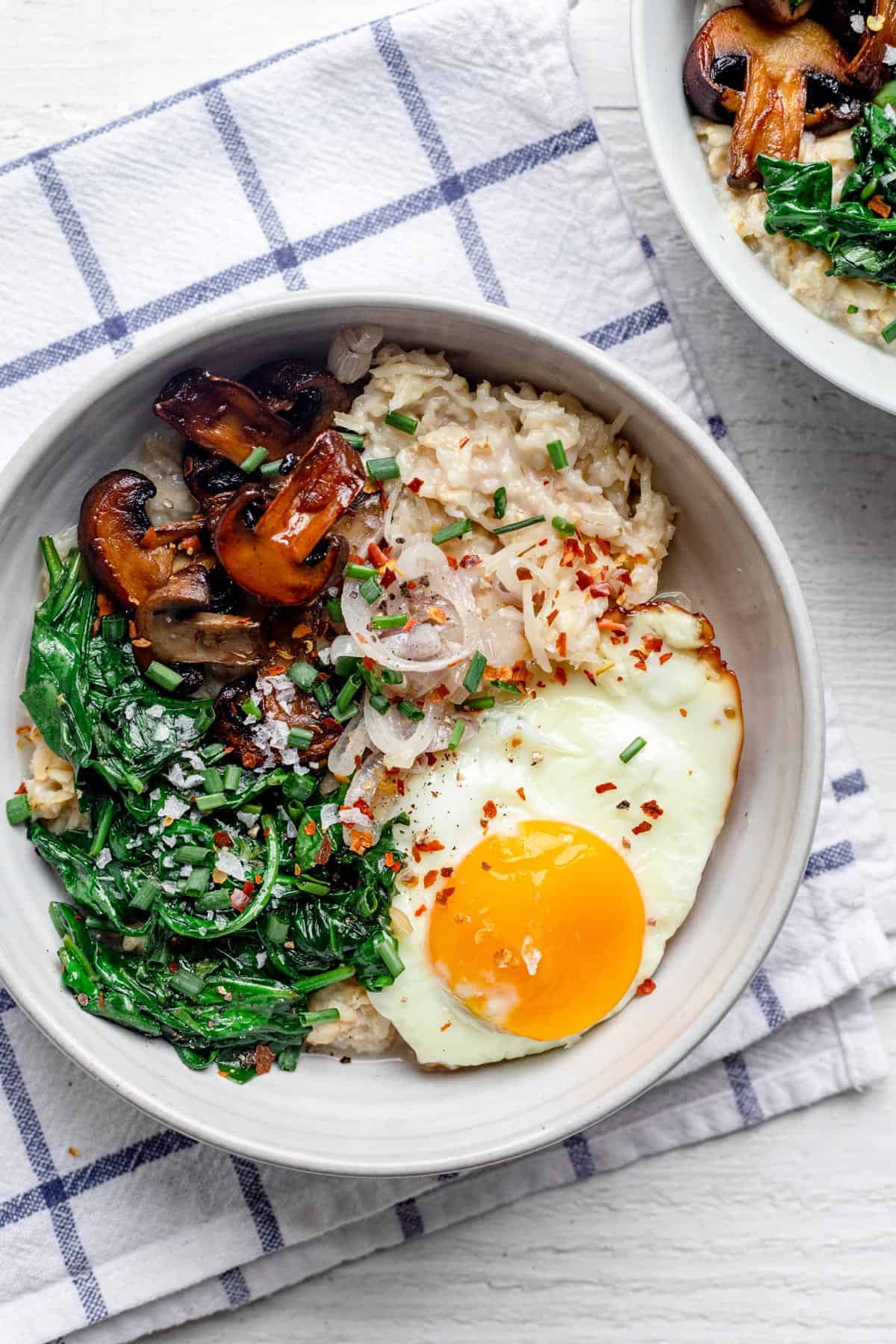 Bowl of savory oatmeal topped with spinach, mushrooms, shallows, and a fried egg