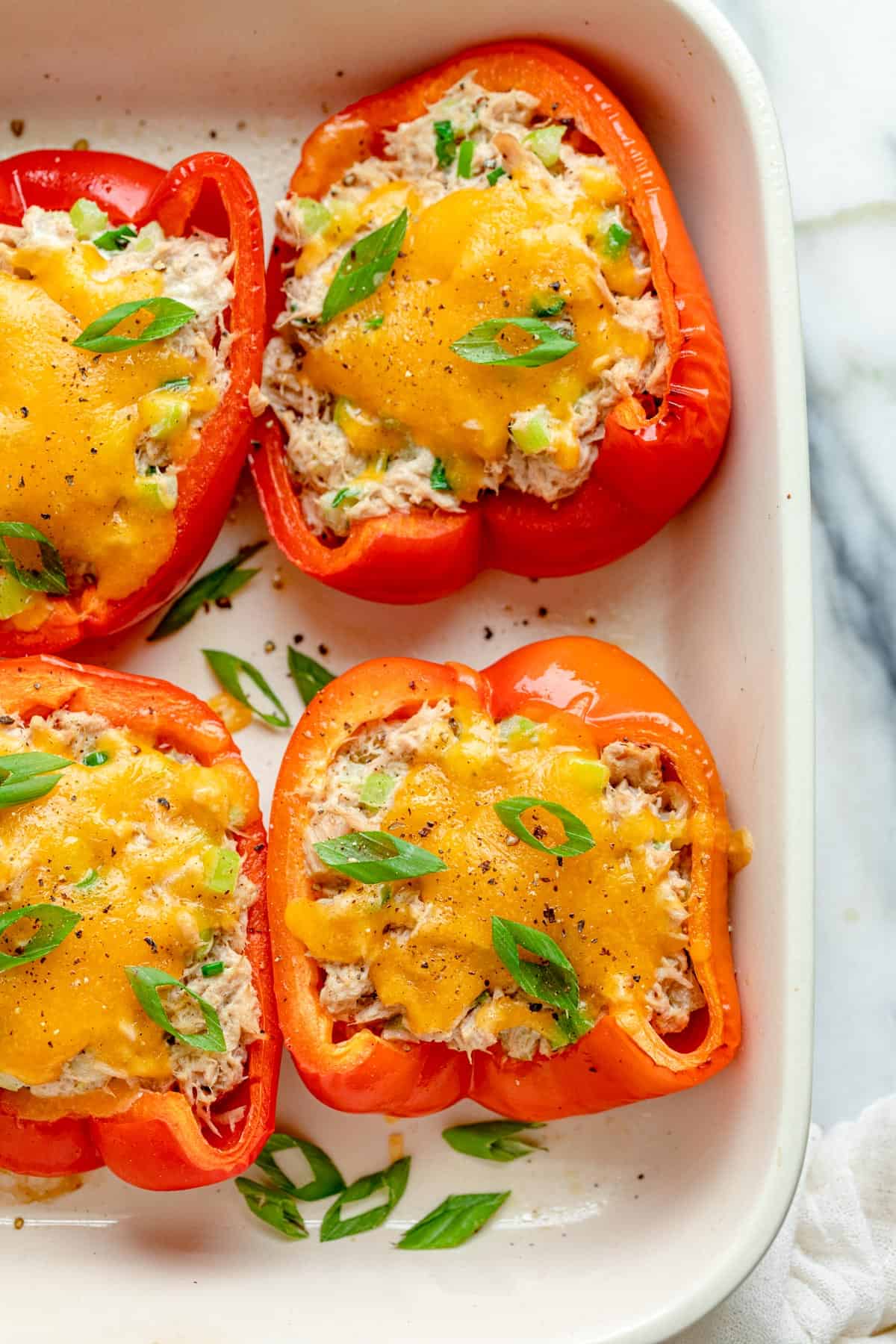 Close up shot of 4 halved bell peppers stuffed with tuna salad and melted cheddar cheese