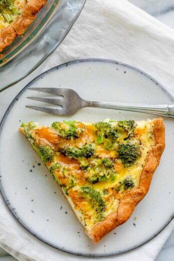 One slice of broccoli and cheese quiche on small plate with fork on the side