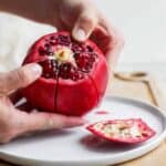 Large pomegranate with top sliced off and hands pulling at the segments
