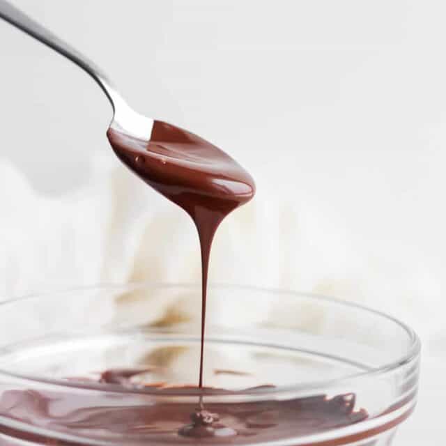 Melted chocolate in a clear glass bowl with spoon dripping