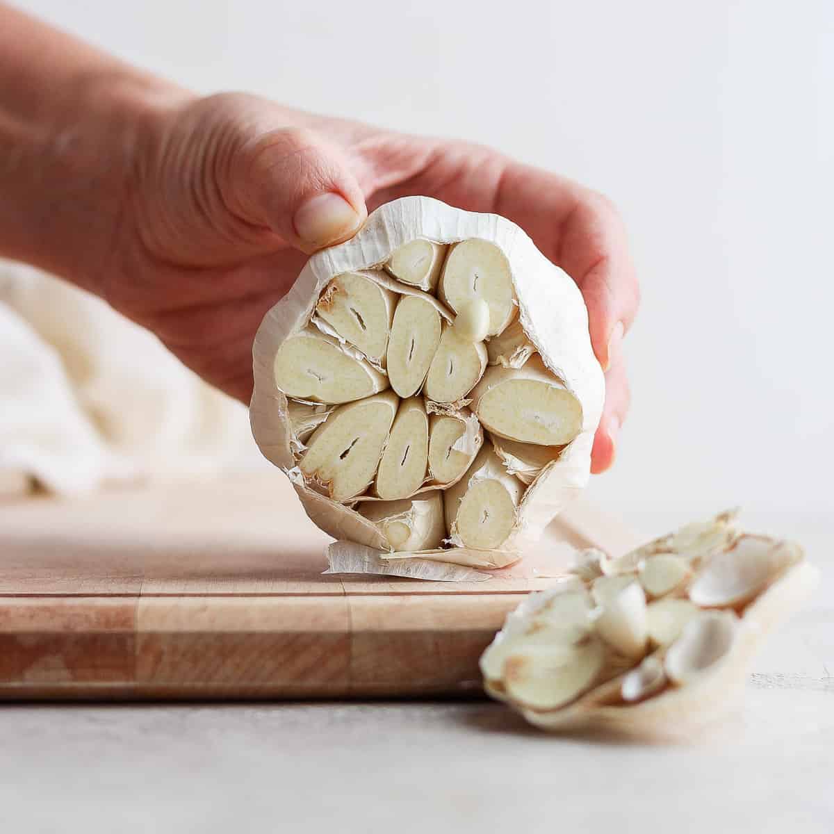 Hand holding head of garlic with top cut off to show the exposed garlic cloves