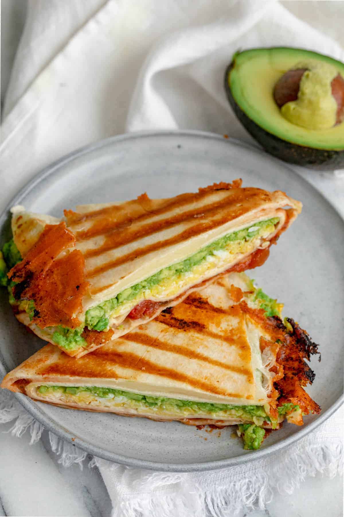 Breakfast tortilla wrap sliced in half on plate with avocado in background