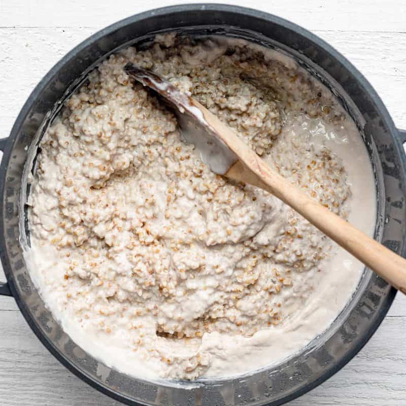 Overnight steel cut oats with milk and water in a pot, being stirred by a wooden spoon.