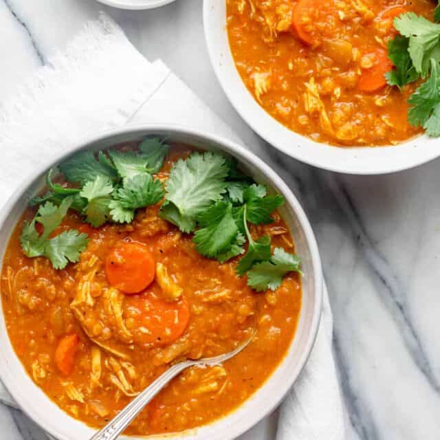 Two bowls of red lentil chicken soup with spoon in one, both topped with cilantro