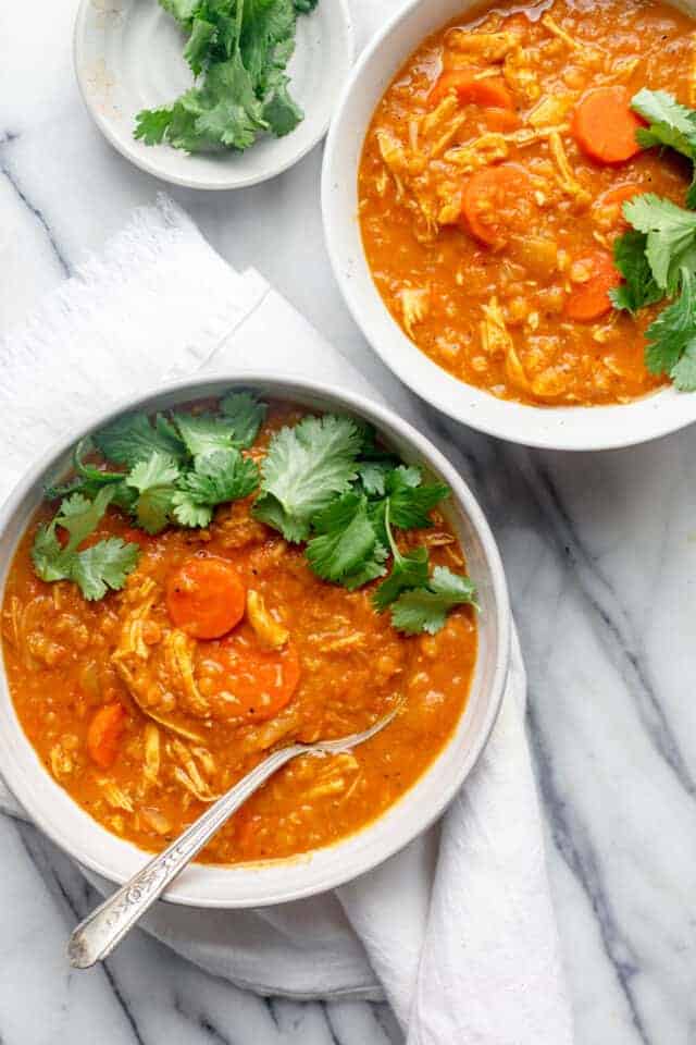 Two bowls of red lentil chicken soup with spoon in one, both topped with cilantro