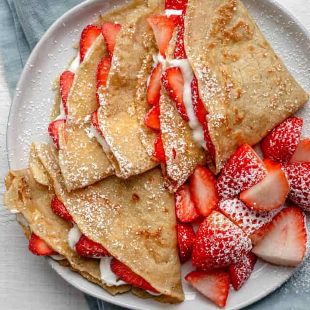 Overhead shot of protein crepes with strawberries and cream on blue napkin