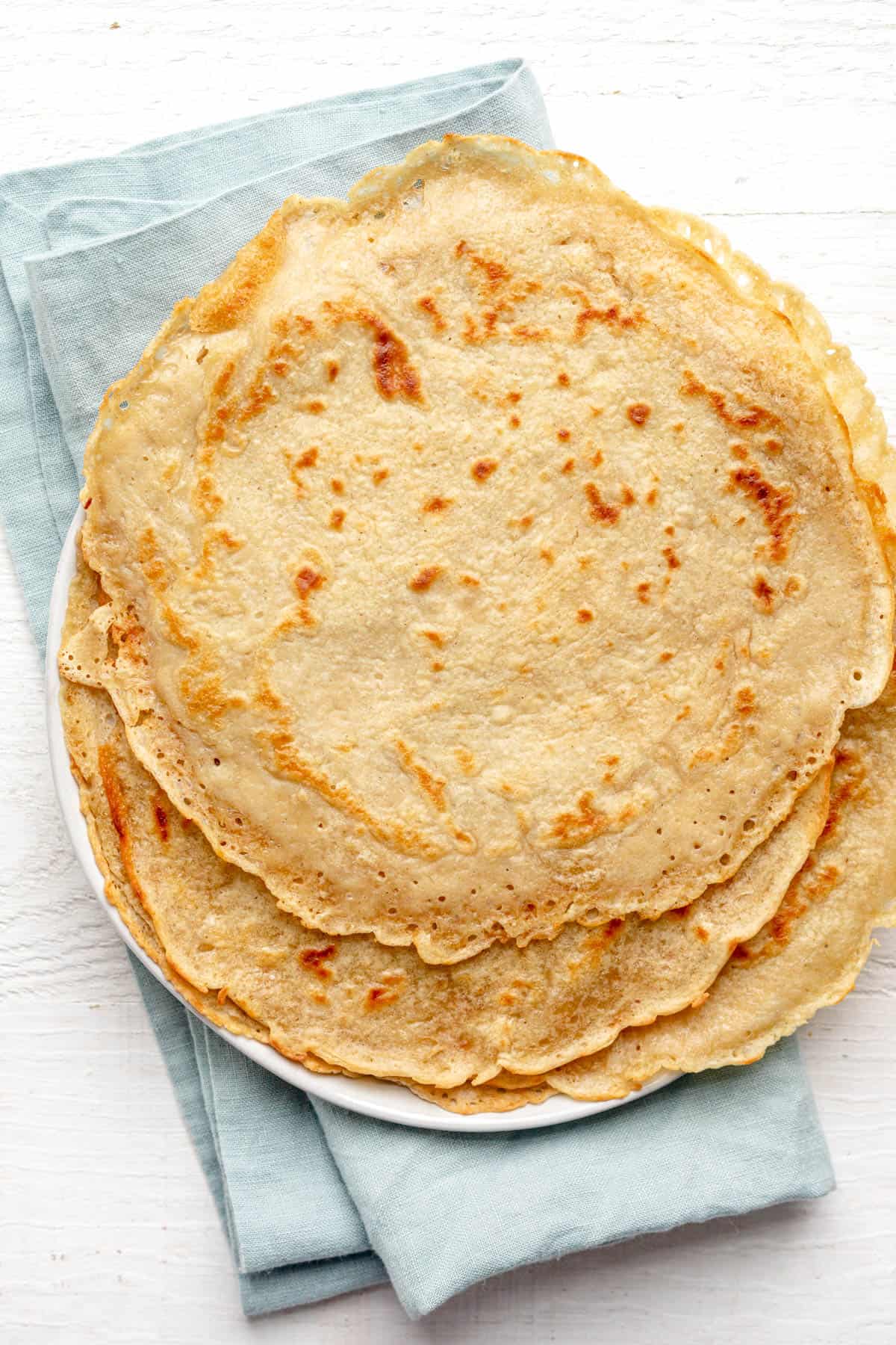 Completed protein crepes stacked on a plate with a blue napkin in background