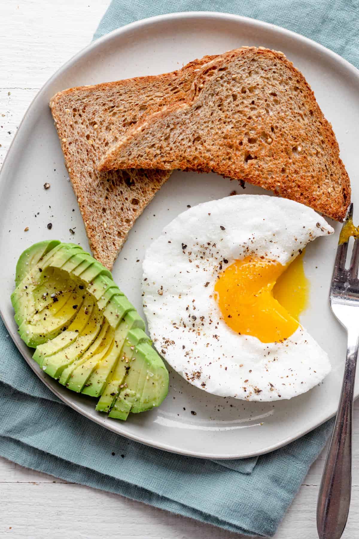 Cutting into cloud egg on a plate with side of toast and avocado