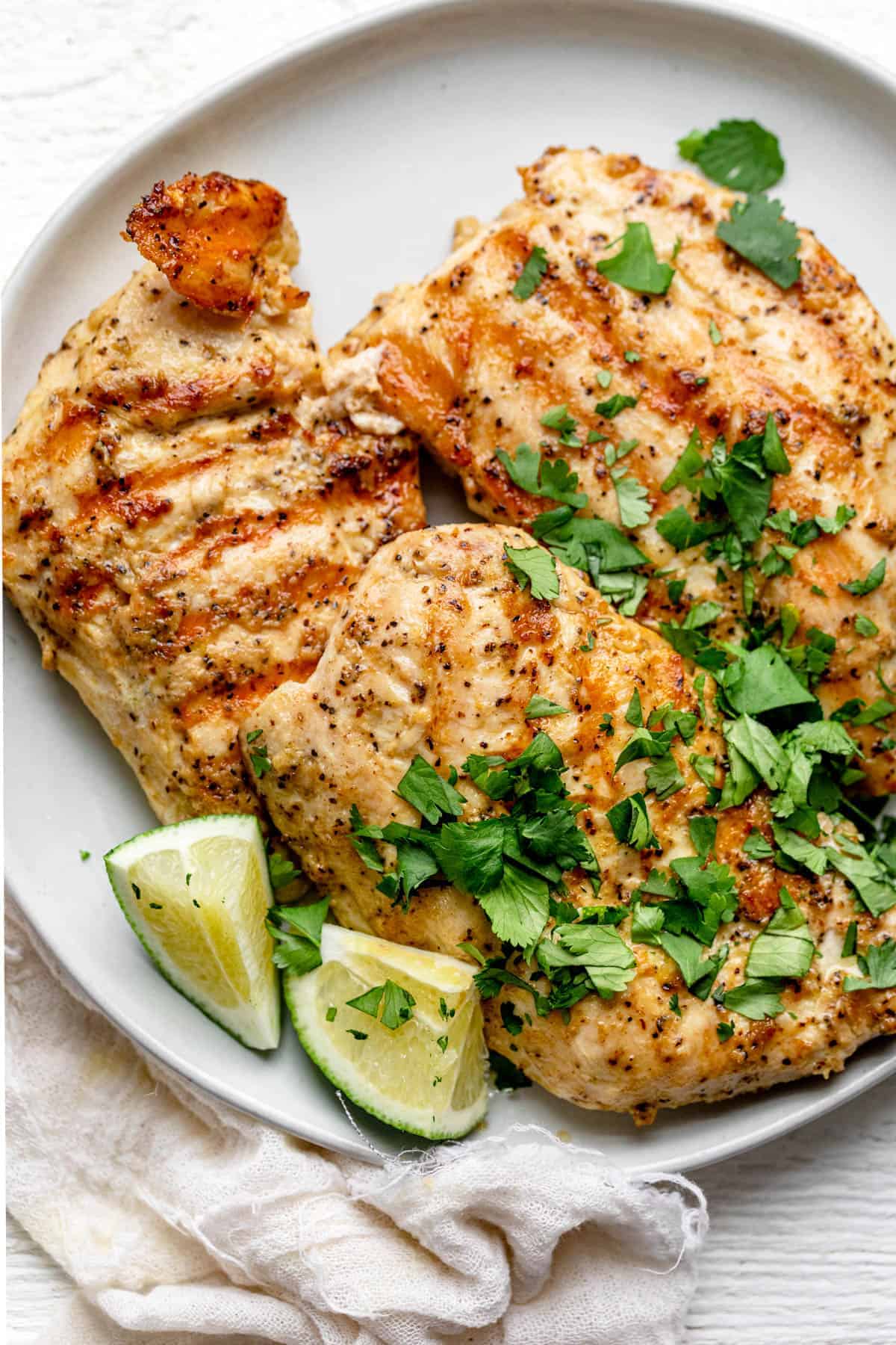 Grilled Dijon chicken on a plate with lime wedges and cilantro