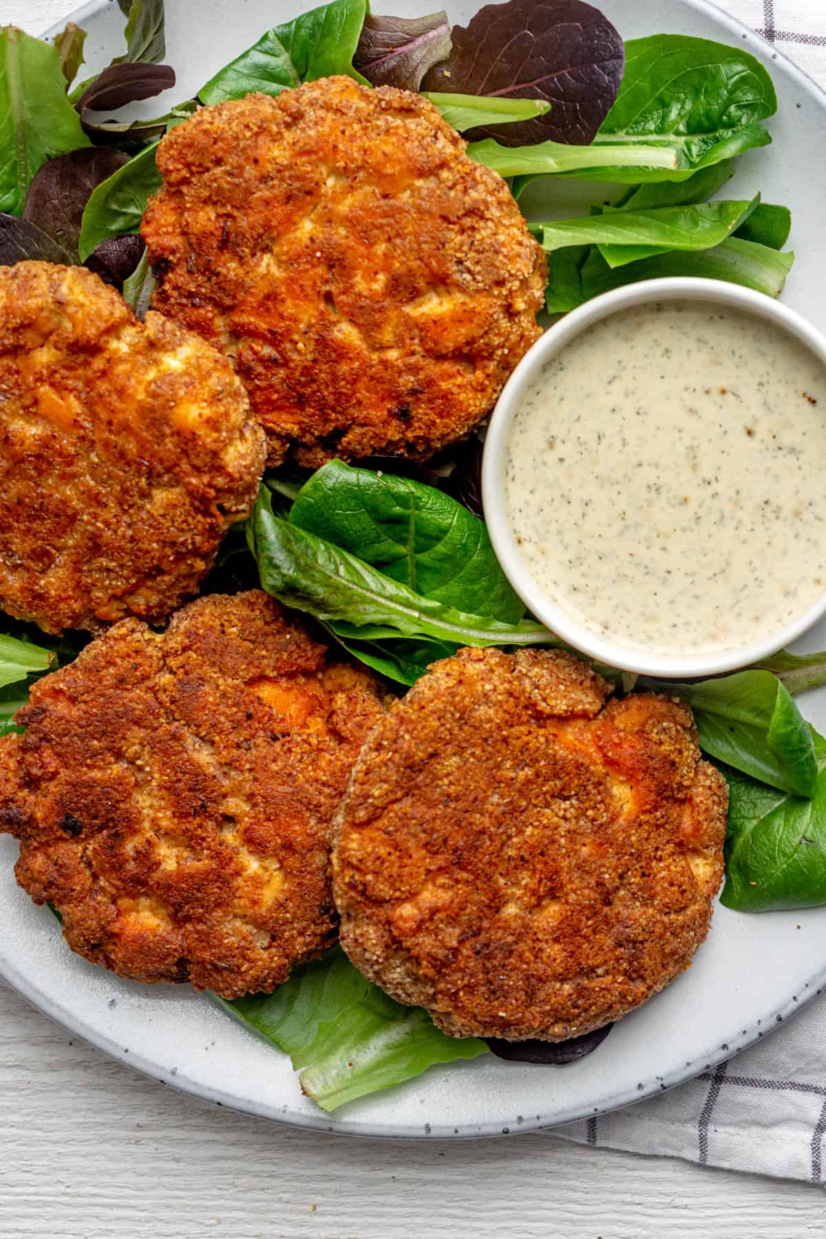 Close up shot of the salmon cakes on bed of greens with dipping sauce