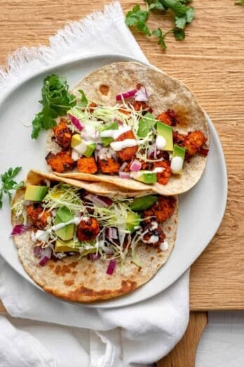 Tempeh tacos on a white plate topped with avocado and cashew cream