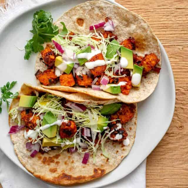 Tempeh tacos on a white plate topped with avocado and cashew cream