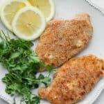 Breaded chicken on plate with parsley and lemon slices