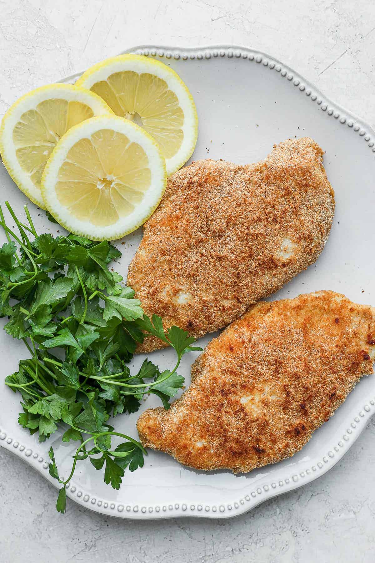Breaded chicken on plate with parsley and lemon slices