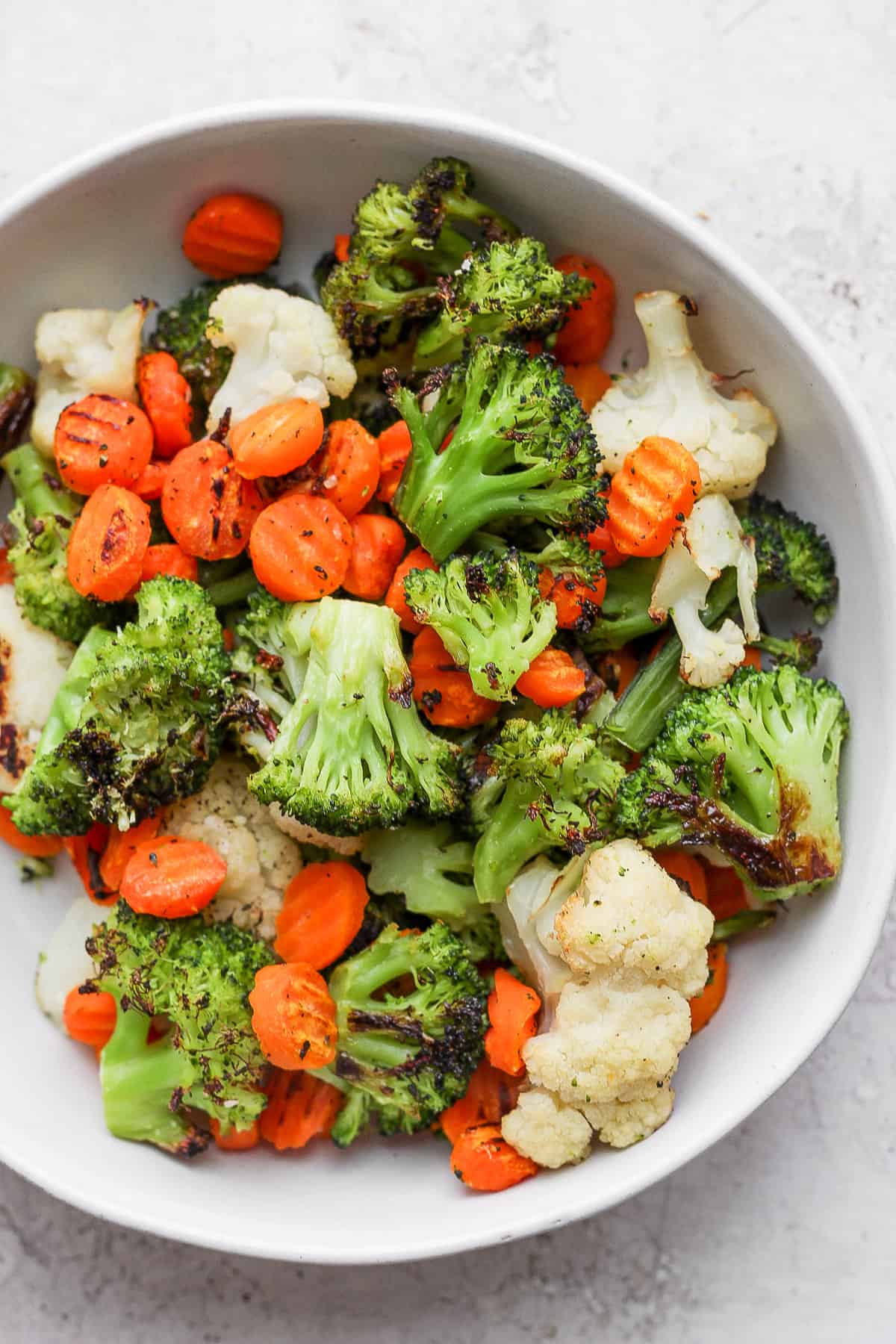 Close up of roasted carrots, broccoli and cauliflower in a large white bowl