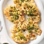 Cauliflower Steaks on a large white plate garnished with chimichurri sauce