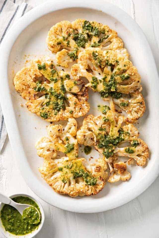 Cauliflower Steaks on a large white plate garnished with chimichurri sauce